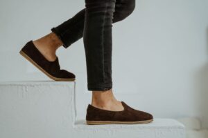 Ben i svarta jeans och bruna loafers på vita trappsteg